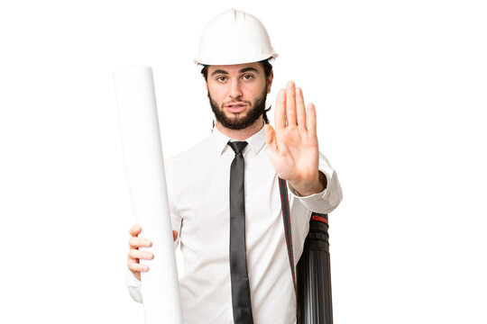Young architect man with helmet and holding blueprints over isolated chroma key background making stop gesture