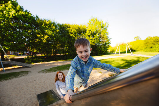 Smiling son climbing on slide with mother in background