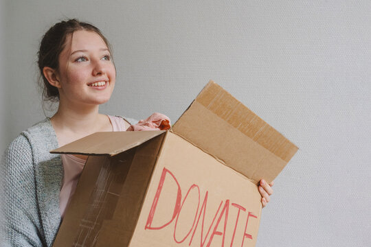 Thoughtful teenage girl with clothes in box for donation by wall
