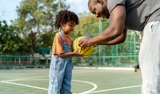Smiling father giving basketball to son on sports court