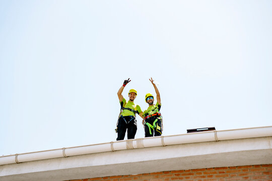 Happy engineers showing victory sign gesture under sky