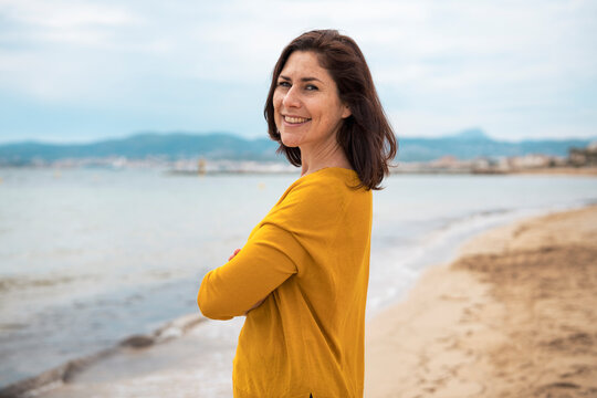 Happy woman standing with arms crossed at beach - Powered by Adobe