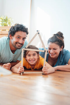 Happy Parents With Daughter Holding Model House On Floor At Home