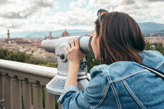 Woman looking through binoculars standing at balustrade