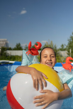 Smiling girl holding ball in swimming pool