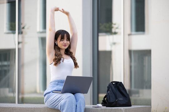 Young woman stretching arms and sitting with laptop on seat
