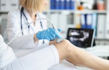 Orthopedic doctor makes ultrasound examination of patient knee in office. Young woman undergoing ultrasound of bones and joints of legs in clinic