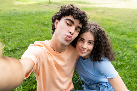 Smiling couple with puckering face taking selfie on grass in park
