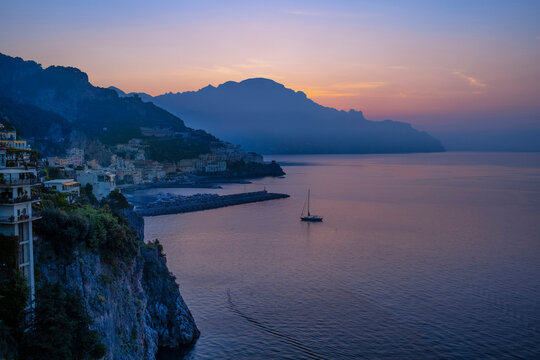 Blue sea with nautical vessel near town at dawn