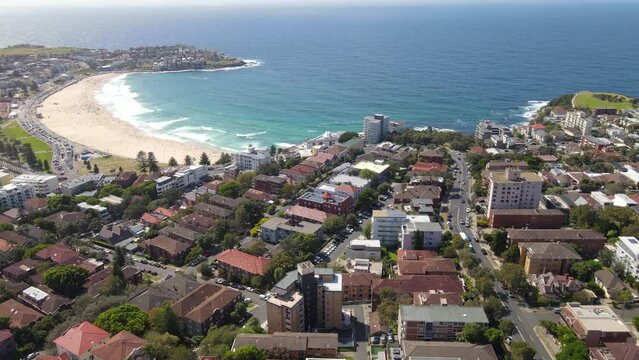 Aerial drone pullback reverse view of homes and streets above the beachside suburbs of Bondi and Tamarama, looking toward Bondi Beach in east Sydney, NSW Australia on a sunny morning