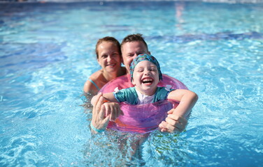 Happy laughing joyful family couple and baby in pool. Family vacation with children in water park