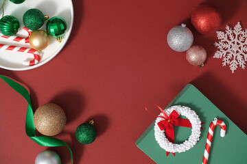 Ideas for decoration on Christmas holiday with cute decorations. Colorful baubles, candy cane, ribbon and gift box arranged on a red background. Top view, scene for advertising with copy space