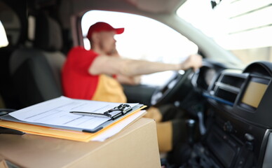 Courier in uniform in car and receipt documents on clipboard for client. Parcel delivery and...