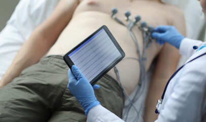 ECG or EKG of heart on tablet of person with electrodes for recording electrocardiogram on bed in...