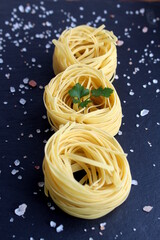 Three spaghetti in the form of a nest lie on a black stone background.