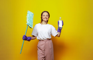 Attractive woman housewife holding mop on bright yellow background