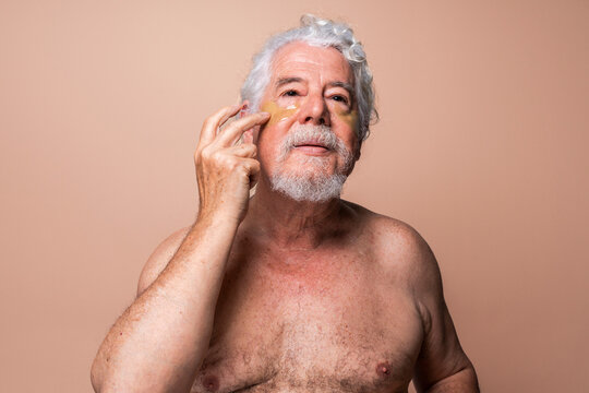 Shirtless senior man applying eye patch against beige background