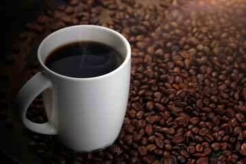 black coffee in white mug with surrounded by roasted coffee beans on dark red wood table