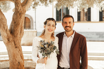 Smiling bride and groom standing near tree