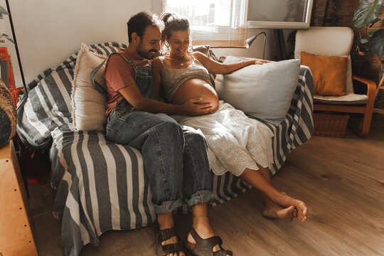 Happy man with pregnant woman sitting on sofa at home