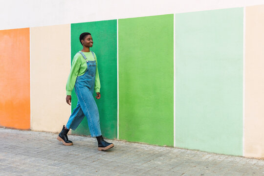 Happy young woman walking in front of multi colored wall at footpath