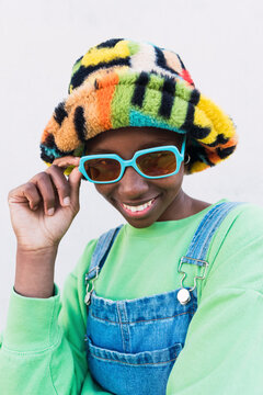 Happy young woman wearing multi colored hat and sunglasses against white background