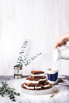 Hand Of Woman Pouring Milk In Cup With Chocolate Cake On Table