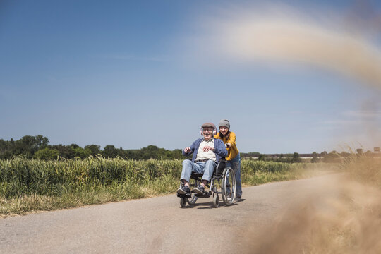 Girl pushing wheelchair with grandfather on sunny day
