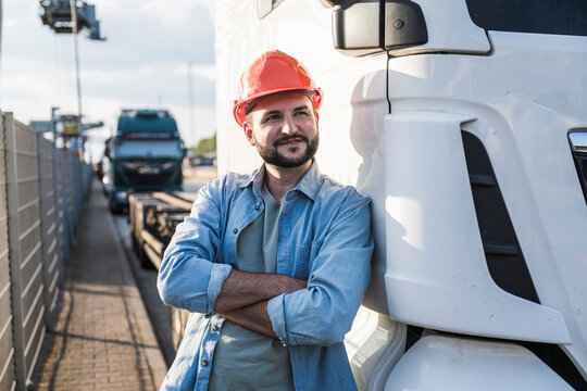 Contemplative truck driver with arms crossed leaning on truck
