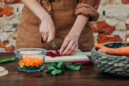 Woman chopping common beet on table in front of brick wall