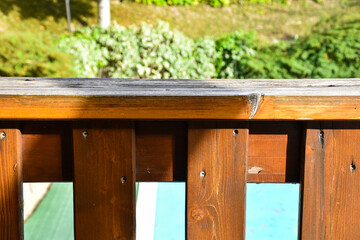 Wooden railing on the terrace outside. Detail on wood with rusty screw. A green landscape and a swimming pool in the background