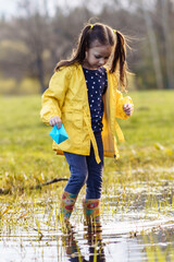 Tranquile child standing in puddle with paper boat in hand and looking at water, preparing to launch ship in fall day.