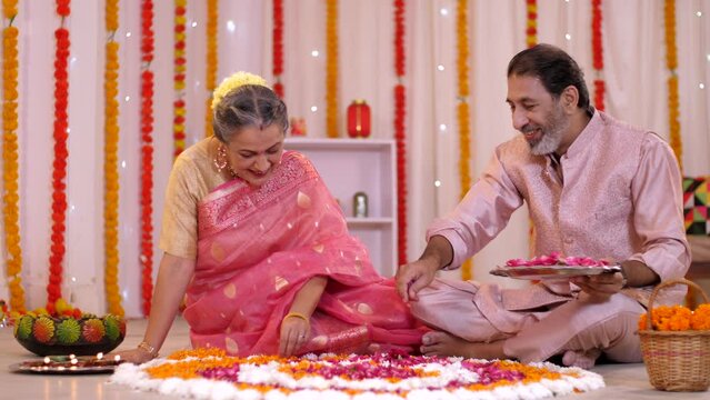 An old-aged Indian couple is decorating a floral Rangoli with rose petals for Diwali. An Indian husband-wife duo preparing for Diwali festival - traditional wear  festive mood  family affair  auspi...