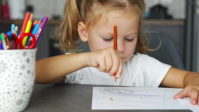 Little girl draws with colored pencils in home. 