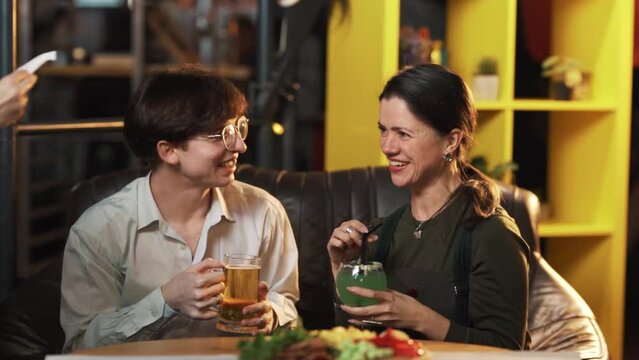 A young beautiful couple is sitting in a bar, drinking beer and cocktails. When the bill arrives, the guy nervously asks to split it, but she refuses and leaves
