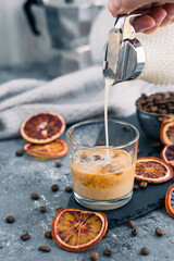 Iced coffee with milk. Summer drink. Pouring milk in coffee with ice cube on grey background