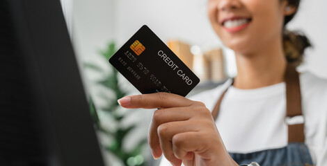 Woman cashier wears an apron and using pos terminal to payment for credit card on coffee shop counter.