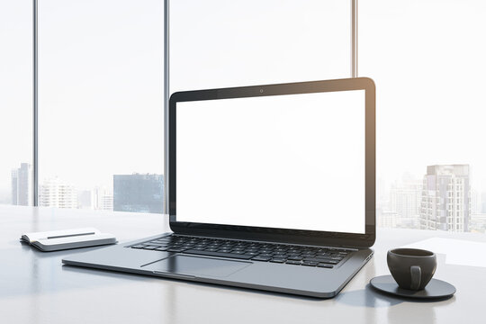 Close up of contemporary workplace with empty white mock up laptop screen, supplies, coffee cup and panoramic window with city view in the background. 3D Rendering.