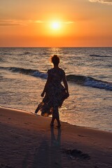 Woman on the seashore in a beautiful evening scenery. Girl walking on the beach with the setting sun in the background. Photo taken at the Baltic Sea in Leba, Poland. - 657007133
