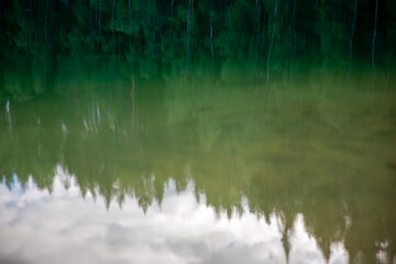 Reflection of trees in the lake with blue sky and white clouds. Reflection of trees in the water. Abstract natural background for design.