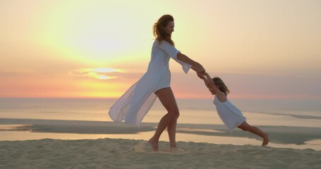 Mother and daughter playing together. Young mother with laughing daughter fooling around at beach during sunset. Young mother having fun while swinging her little girl at sunset - Powered by Adobe