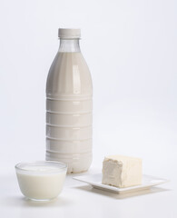 fresh milk in plastic bottle with yogurt in glass bowl and soft cheese on white plate with white background