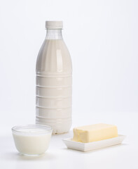 fresh milk in plastic bottle with yogurt in glass bowl and fresh butter on white plate with white background