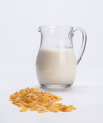 fresh milk in glass jug with cornflakes in the foreground resting on the white background