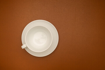 Top view of an empty white coffee cup on a brown background.