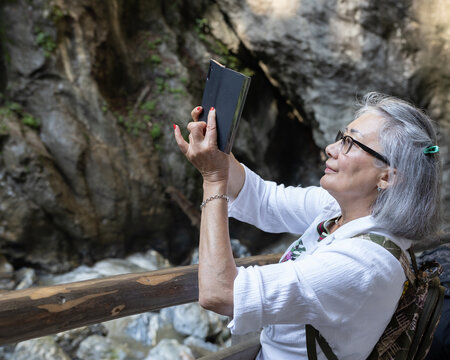 Adult oriental woman with gray hair taking a video shoot in Liechtensteinklamm National Park, Austria