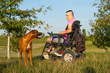 Brown dog looks at man wearing pink t-shirt in wheelchair with leg injury after car accident. Owner...