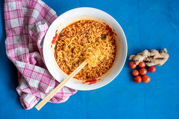 flat lay image of prepared spicy noodles in a ceramic bowl, ginger and tomatoes around it- food concept