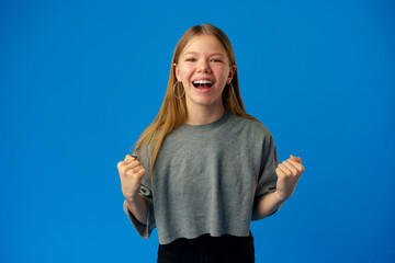 Portrait of a joyful happy teenage girl celebrating success on blue background