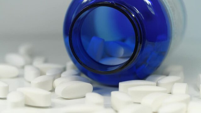 Big white pills scattered on table. Overdose. Open blue container for nutritional supplements lies on table. In reality these are biologically active sulfur pills in dosage of 1500 mg. MSM for joints